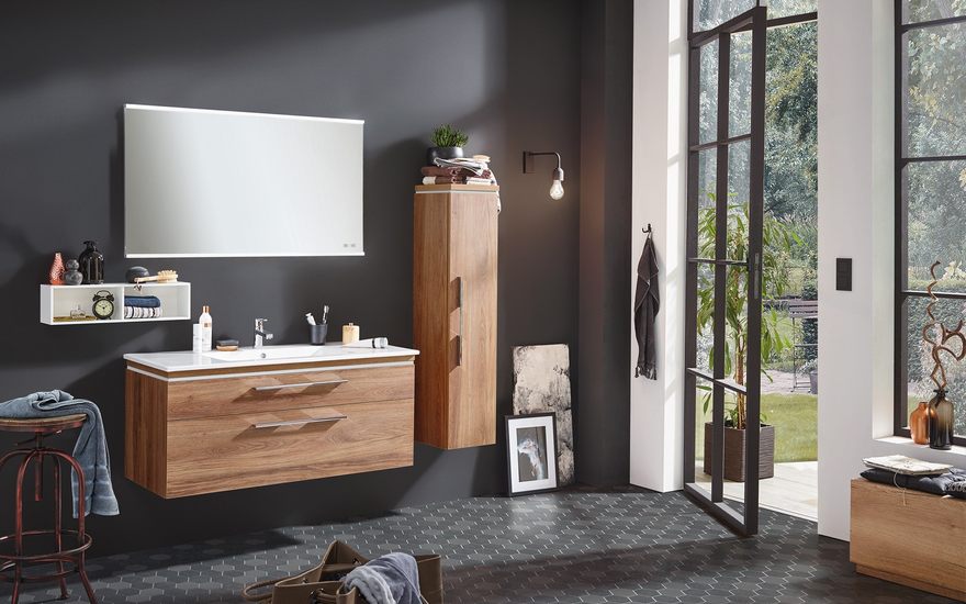 Braune Badezimmermöbel mit einem beleuchteten Spiegel in einem grauen Badezimmer